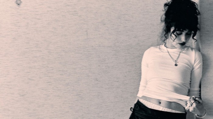 A woman with dark curly hair leaning against a wall